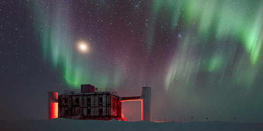 The IceCube neutrino observatory at night with aurorae at the sky