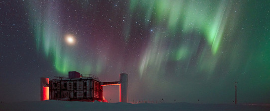 The IceCube neutrino observatory at night with aurorae at the sky